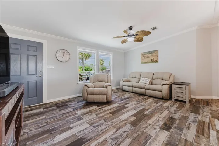 Living room with wood finished floors, a ceiling fan, baseboards, and crown molding