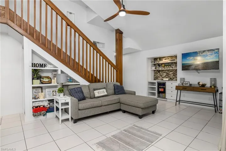 Great Room with Vaulted Ceiling, Tile Floors, Built-In Shelving Under Stairway, Built-In Dry Bar with Tiled Backsplash, Shelving, Drawer Storage, & Beverage Fridge, & Stairway to Second Floor Loft