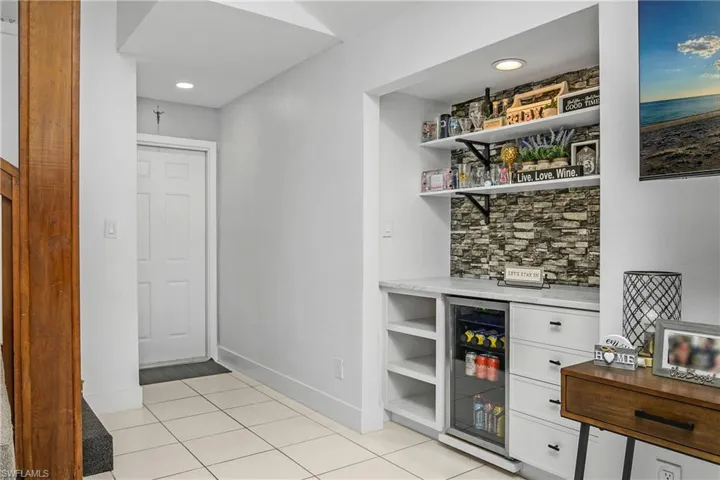 Front Hallway with Built-In Dry Bar with Tiled Backsplash, Shelving, Drawer Storage, & Beverage Fridge, Recessed Lighting, Stairway to Second Floor Loft, & Front Entry Door