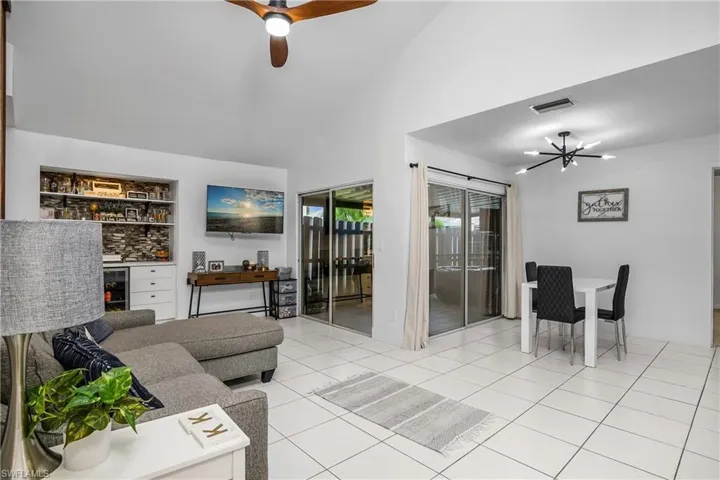 Great Room with Vaulted Ceiling, New Ceiling Fan, Dining Area with New Modern Light Fixture, Sliding Doors to the Screened-In & Fenced Lanai, & Built-In Dry Bar with Tile Backsplash, Shelving, Drawer Storage, & Beverage Fridge