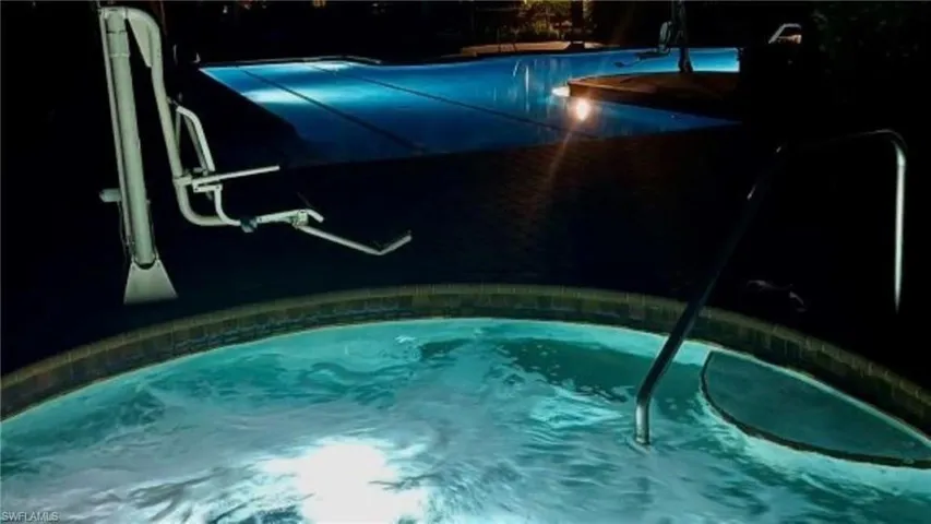 Illuminated spa and pool area with a built-in pool lift, integrated steps, and surrounding coping
