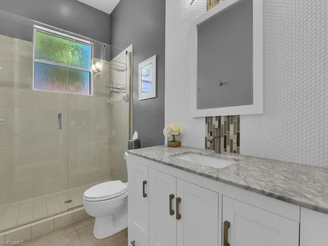 Bathroom featuring a shower stall, vanity, light tile patterned floors, and decorative backsplash