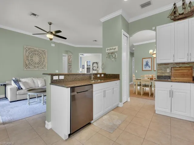 Kitchen with dark stone counters, arched walkways, white cabinets, crown molding, and dishwasher