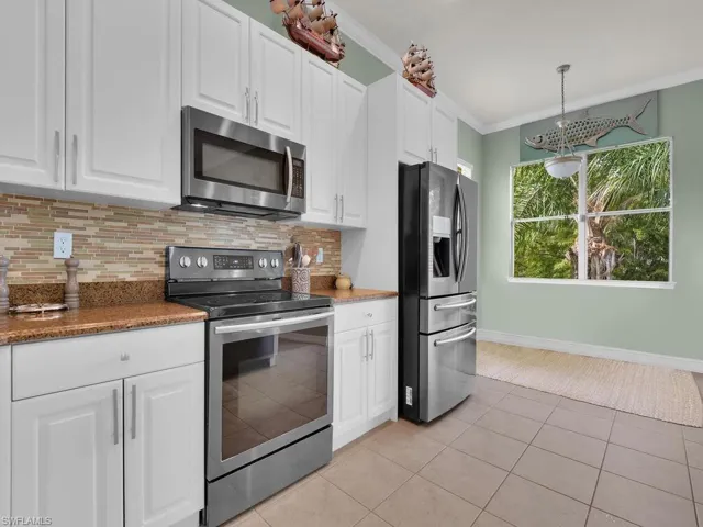 Kitchen with appliances with stainless steel finishes, white cabinetry, ornamental molding, and light tile patterned floors