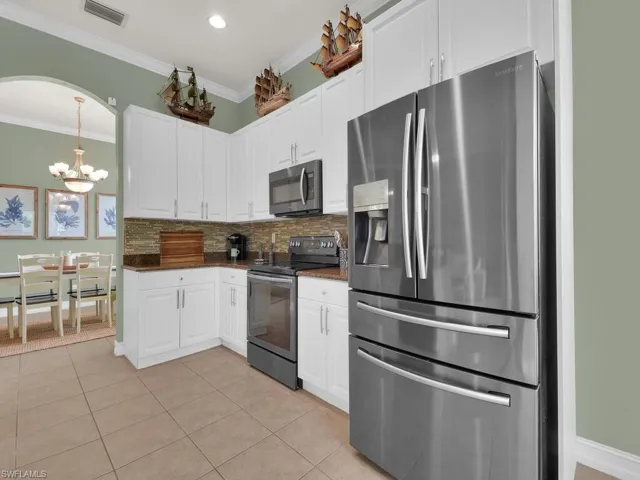 Kitchen featuring stainless steel appliances, light tile patterned floors, crown molding, white cabinets, and a chandelier