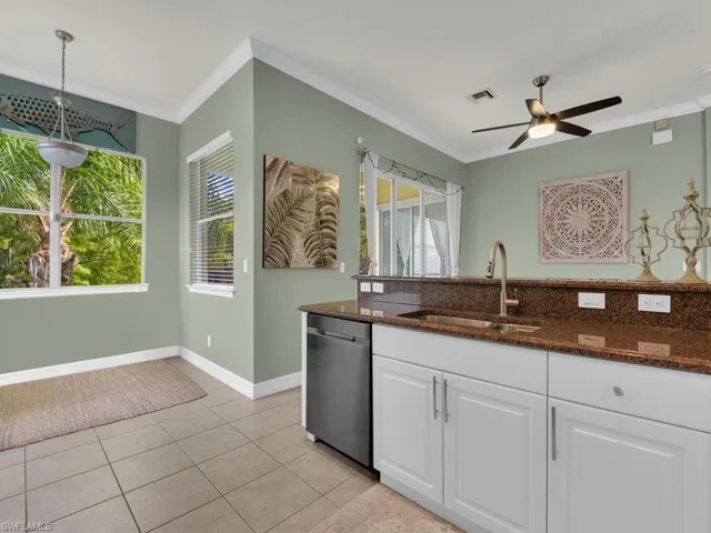 Kitchen featuring dark stone countertops, white cabinets, ornamental molding, light tile patterned flooring, and dishwashing machine