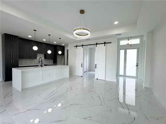 Kitchen featuring a barn door, light marble finish flooring, a raised ceiling, recessed lighting, and dark cabinets