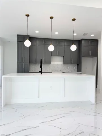 Kitchen featuring light marble finish floors, backsplash, a kitchen island with sink, decorative light fixtures, and recessed lighting