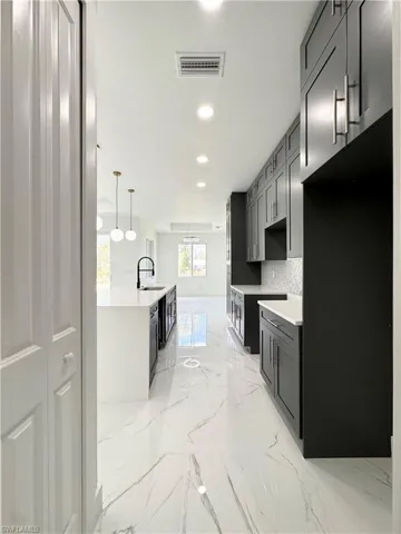 Kitchen with light marble finish floors, recessed lighting, decorative backsplash, a kitchen island with sink, and pendant lighting