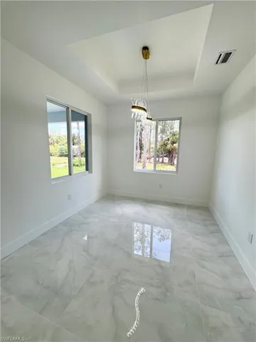 Unfurnished room with a raised ceiling, recessed lighting, and light marble finish flooring