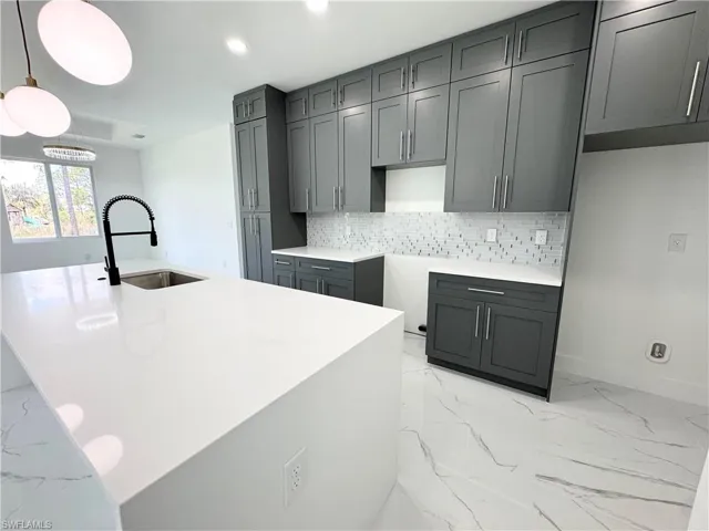 Kitchen with tasteful backsplash, light marble finish floors, decorative light fixtures, an island with sink, and recessed lighting