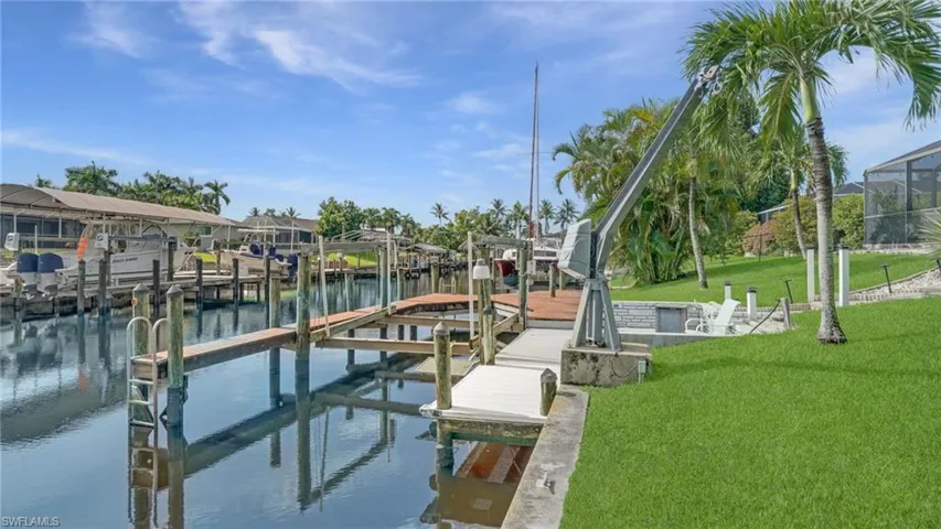 Dock area with boat lift, a water view, and a lawn