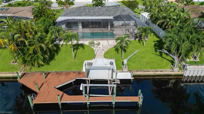 Dock area featuring a water view, boat lift, an outdoor pool, glass enclosure, and a yard