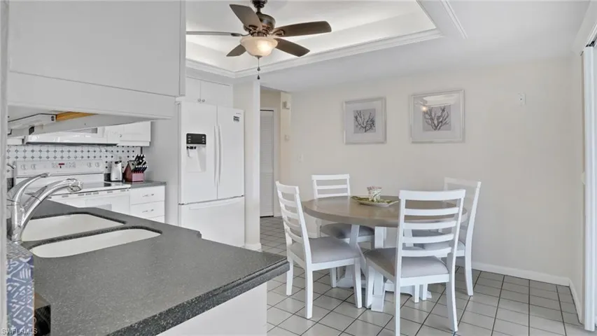 Dining area with a tray ceiling, a ceiling fan, and light tile patterned floors