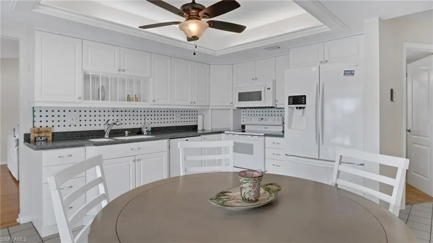 Kitchen featuring dark countertops, white appliances, white cabinets, and decorative backsplash