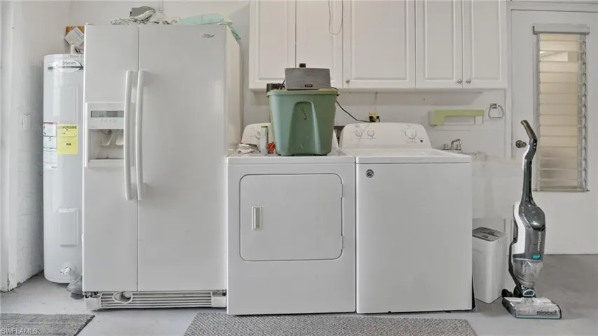 Laundry room featuring concrete floors, water heater, washer and dryer, and cabinet space