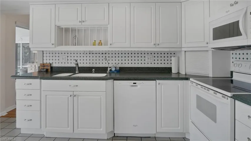 Kitchen with white appliances, decorative backsplash, white cabinets, dark countertops, and open shelves
