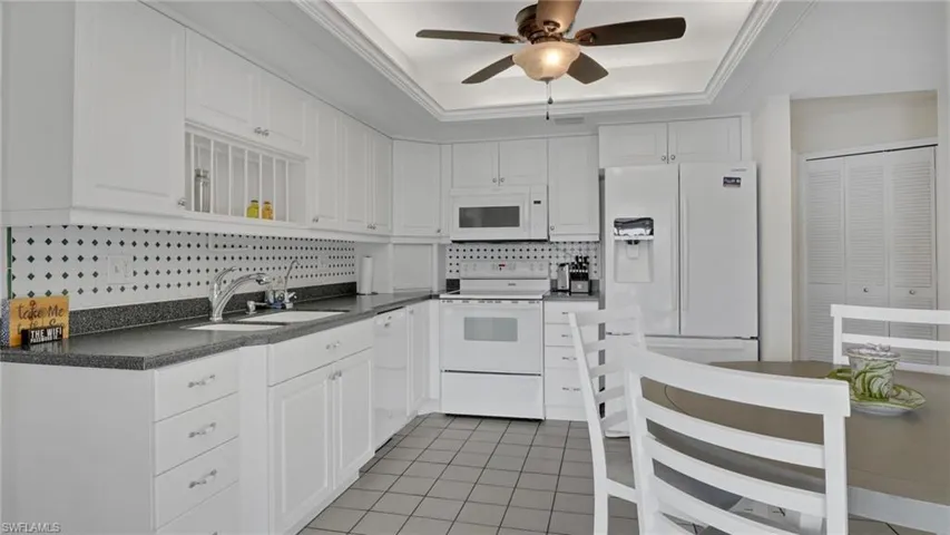 Kitchen with white appliances, dark countertops, white cabinetry, and crown molding