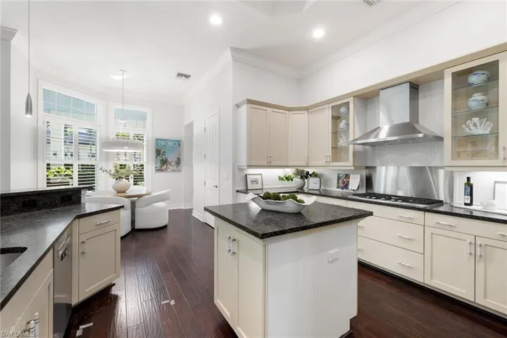 Kitchen featuring ornamental molding, wall chimney exhaust hood, pendant lighting, a kitchen island, and dark wood finished floors