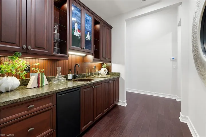Bar featuring dark stone counters, dishwasher, glass insert cabinets, dark brown cabinets, and dark wood-type flooring