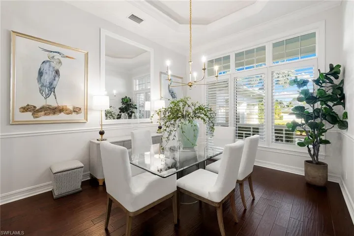 Dining area with ornamental molding, a raised ceiling, dark wood finished floors, and a chandelier