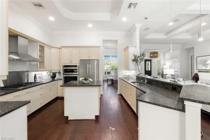 Kitchen featuring stainless steel appliances, wall chimney exhaust hood, cream cabinets, dark stone countertops, and recessed lighting