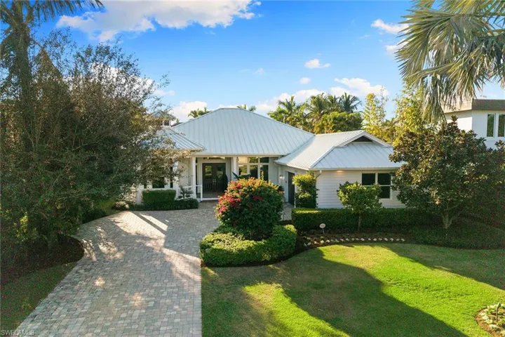 View of front of property with a porch, decorative driveway, a front yard, and a metal roof