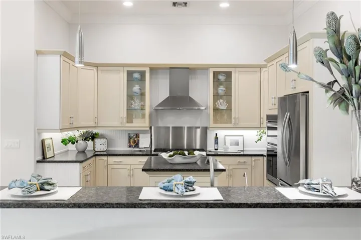 Kitchen with decorative light fixtures, wall chimney exhaust hood, cream cabinets, stainless steel appliances, and crown molding