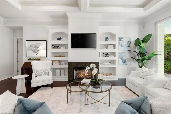 Living room featuring a lit fireplace, ornamental molding, built in shelves, wood finished floors, and beam ceiling