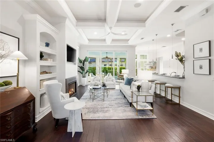 Living room with dark wood-type flooring, a lit fireplace, beam ceiling, coffered ceiling, and built in shelves