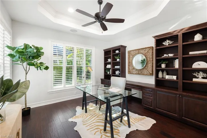 Home office with crown molding, ceiling fan, dark wood-style flooring, and a tray ceiling