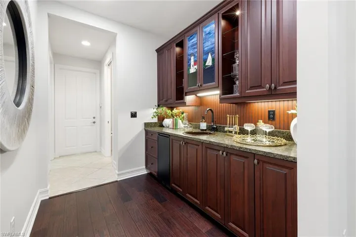 Bar area featuring glass insert cabinets, dark wood-style flooring, dark brown cabinets, dark stone counters, and recessed lighting