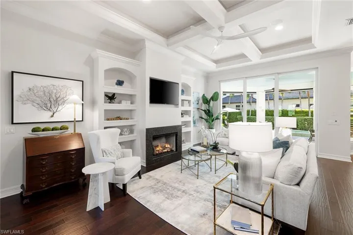 Living room featuring coffered ceiling, built in features, crown molding, beamed ceiling, and hardwood / wood-style floors