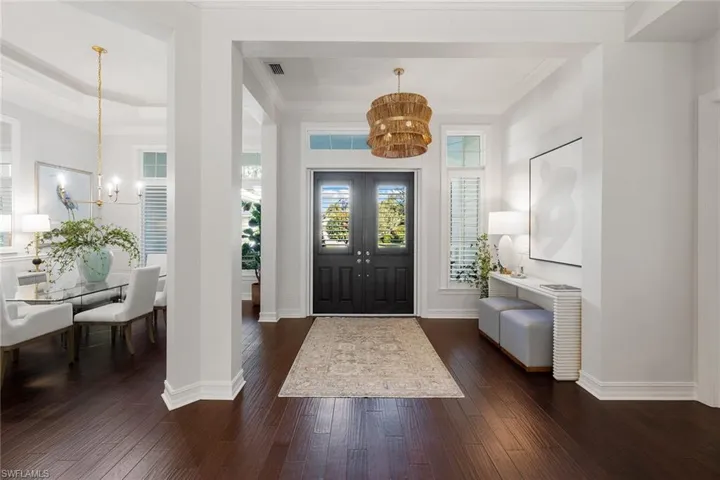 Foyer entrance with a chandelier, crown molding, and dark wood finished floors