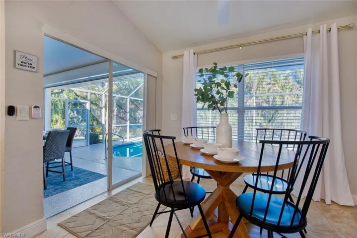Dining area with healthy amount of natural light, a sunroom, light tile patterned flooring, and vaulted ceiling