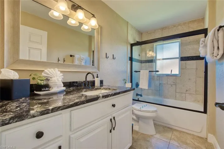Full bath featuring vanity, bath / shower combo with glass door, light tile patterned flooring, and a textured wall