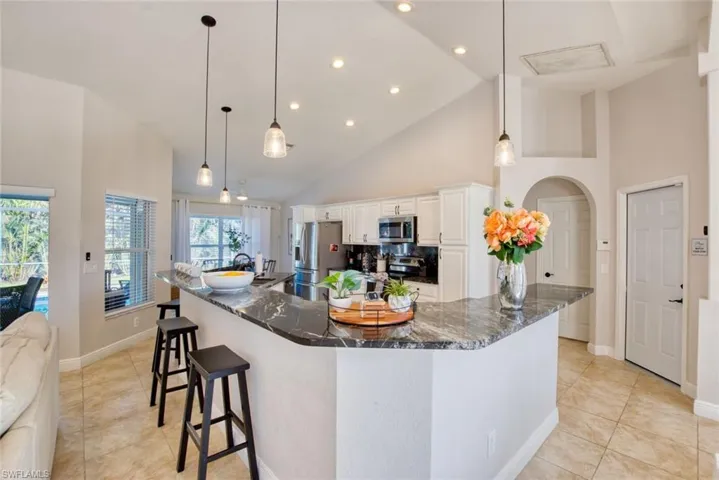 Kitchen with high vaulted ceiling, recessed lighting, white cabinetry, stainless steel appliances, and dark stone countertops