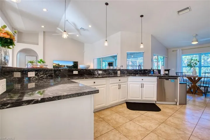 Kitchen featuring ceiling fan, white cabinetry, high vaulted ceiling, stainless steel dishwasher, and hanging light fixtures