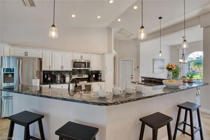 Kitchen with white cabinetry, backsplash, dark stone countertops, a kitchen breakfast bar, and appliances with stainless steel finishes