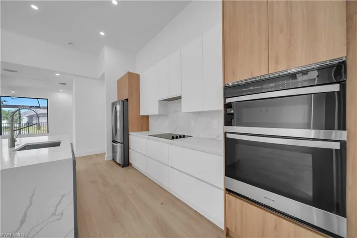 Kitchen with stainless steel appliances, modern cabinets, light wood-type flooring, backsplash, and recessed lighting