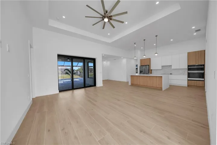 Unfurnished living room with a tray ceiling, ceiling fan, recessed lighting, light wood-type flooring, and a towering ceiling