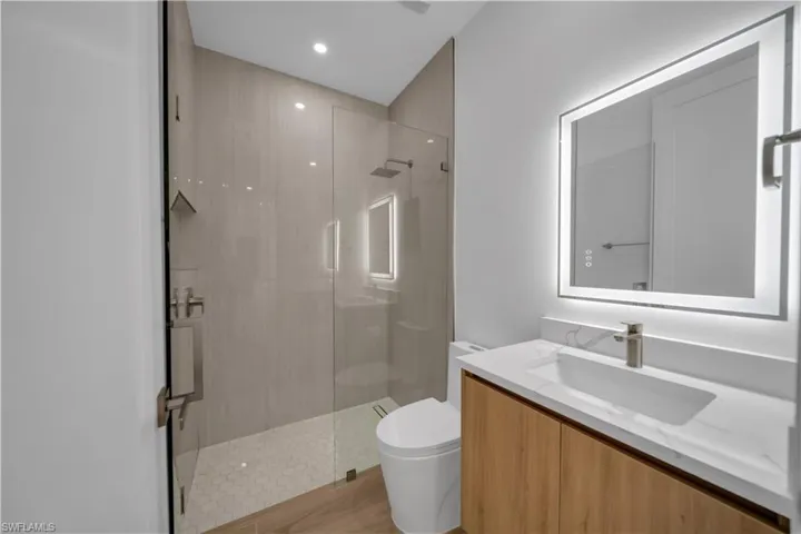 Full bathroom with tiled shower, vanity, recessed lighting, and wood finished floors
