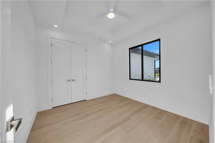 Unfurnished bedroom with light wood-style floors, a tray ceiling, recessed lighting, a closet, and a ceiling fan