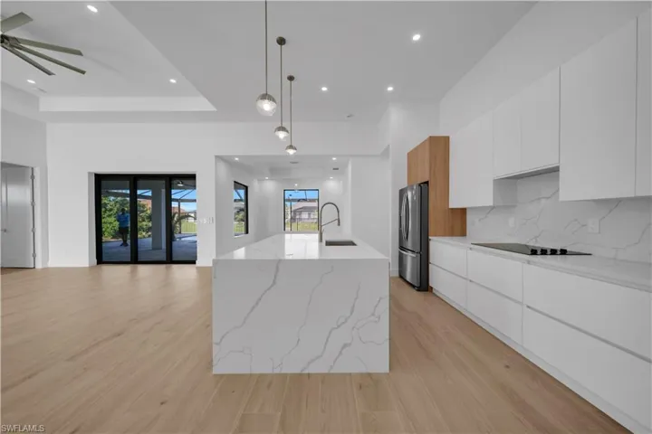 Kitchen with modern cabinets, freestanding refrigerator, black electric stovetop, and recessed lighting
