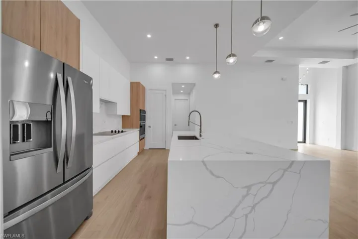 Kitchen featuring stainless steel appliances, modern cabinets, light wood finished floors, a center island with sink, and recessed lighting