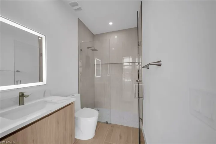 Bathroom with a stall shower, vanity, wood finished floors, and recessed lighting