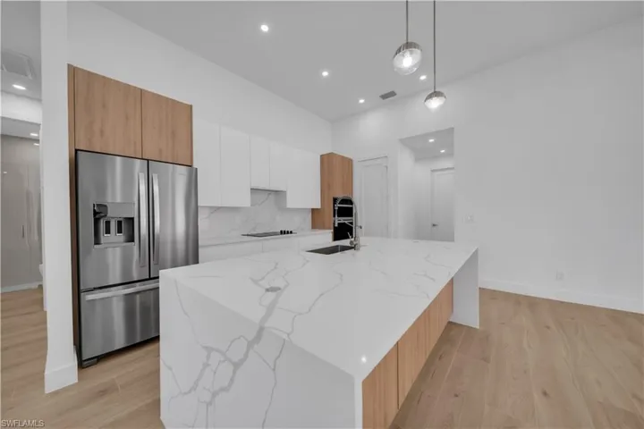 Kitchen with stainless steel fridge, modern cabinets, white cabinets, light wood finished floors, and recessed lighting