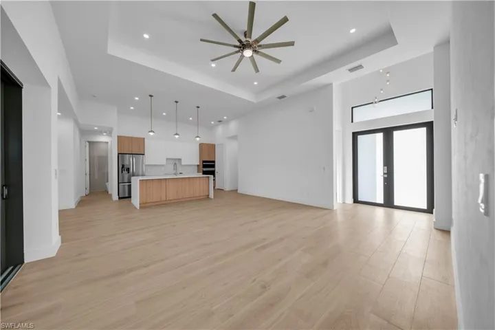 Unfurnished living room featuring a tray ceiling, recessed lighting, a ceiling fan, light wood-style flooring, and a high ceiling