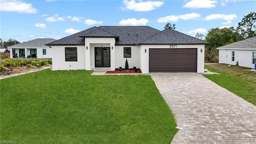 View of front facade with a front yard, stucco siding, an attached garage, and decorative driveway