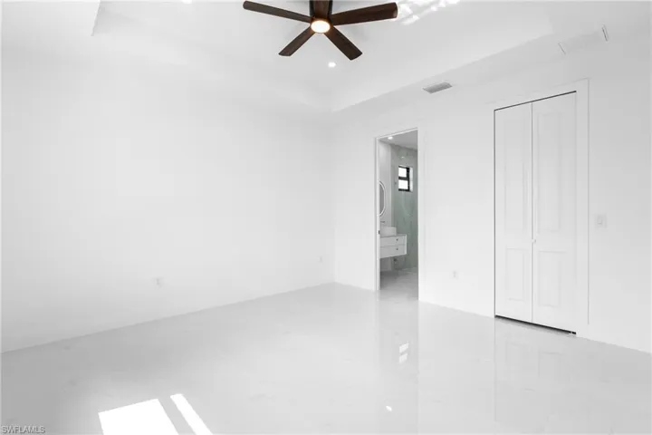 Unfurnished bedroom featuring a tray ceiling, ensuite bathroom, a ceiling fan, and recessed lighting